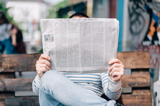 Man is sitting on a bench reading a newspaper.
